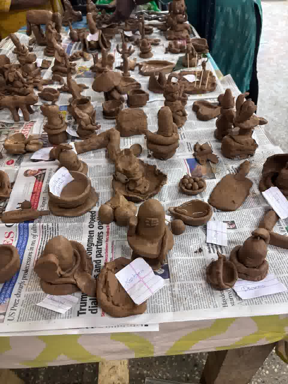 Newly made clay figures, including Ganesha and Shiva lingam idols, bowls and diyas, laid out on newspaper with name slips