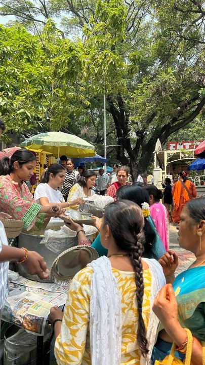 Volunteers ladling hot food from steel vessels into plates held out by people in line