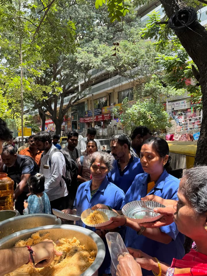 Volunteers handing out plates of rice to a crowd gathered around the serving pots