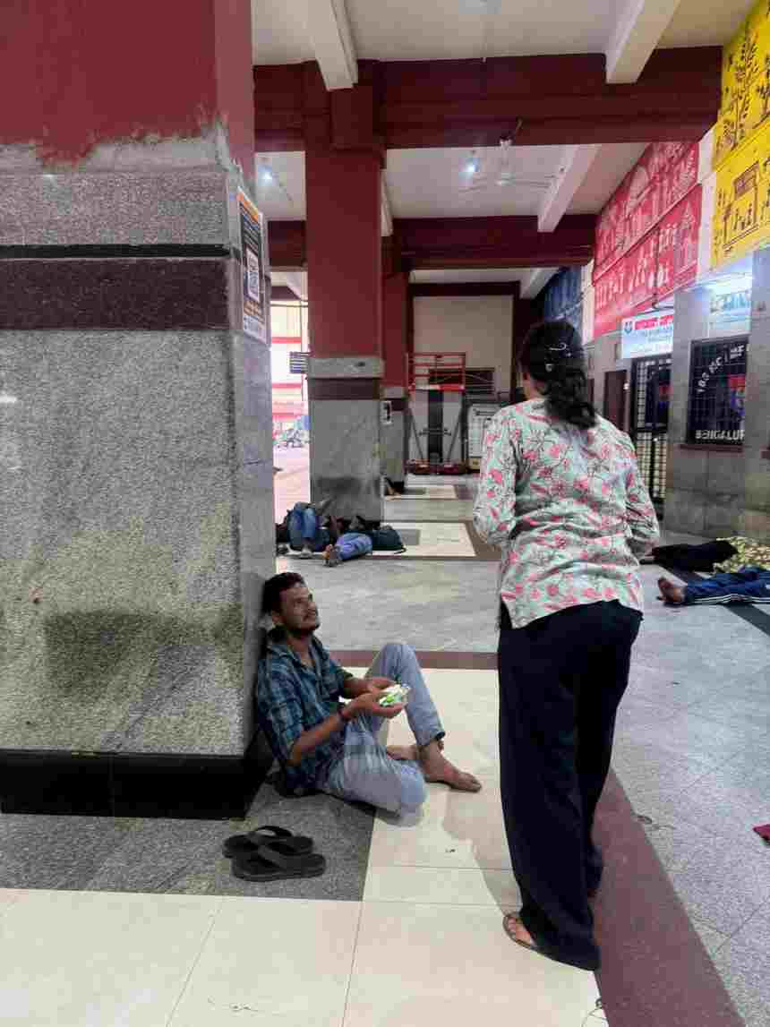 A volunteer handing a food box to a man seated on the floor of the railway station